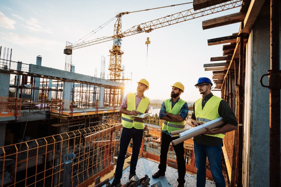 A group of construction workers discussing and inspecting a job with cranes in the background