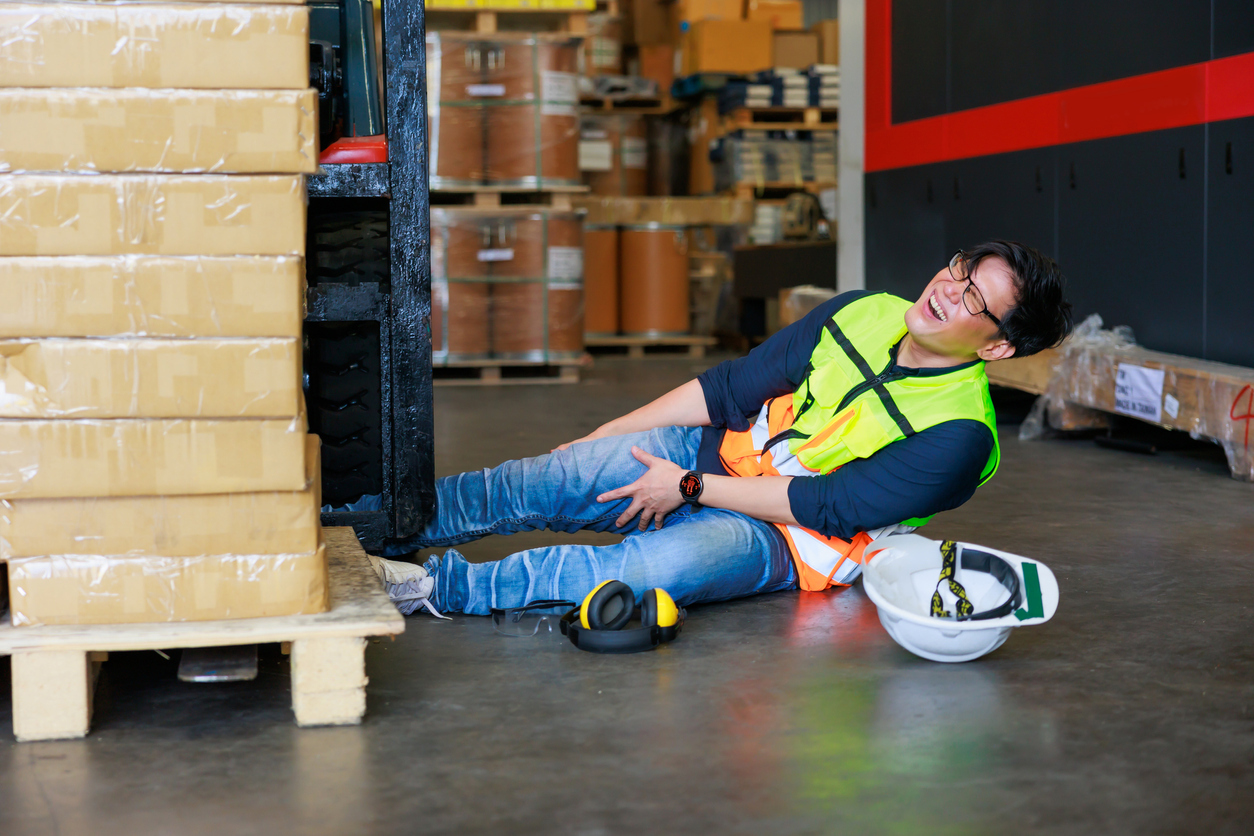 A warehouse worker lying on the floor grasping his leg after an injury