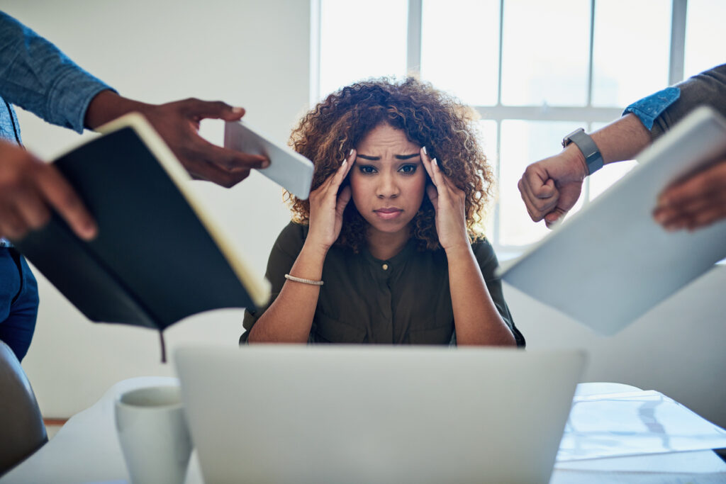 A stressed out woman sitting in front a laptop holding her head with hands reaching to give her more work