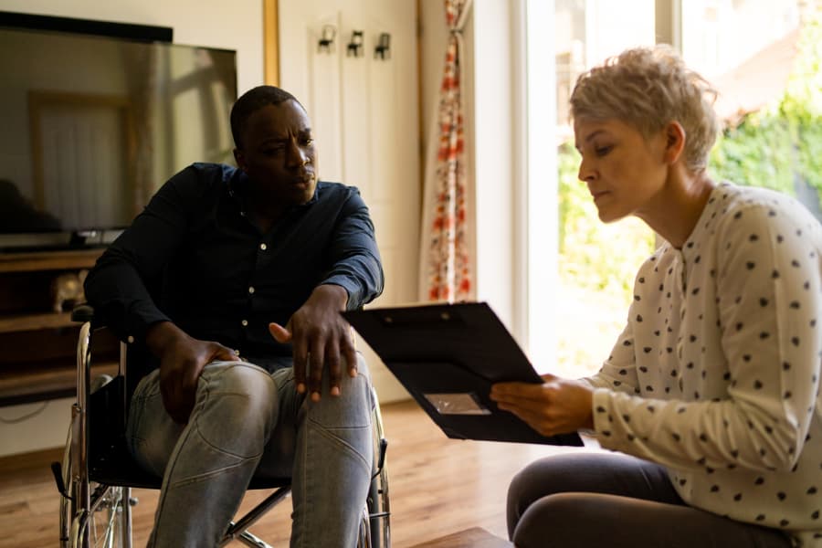 A female social worker holding a clipboard while talking to a man in a wheelchair