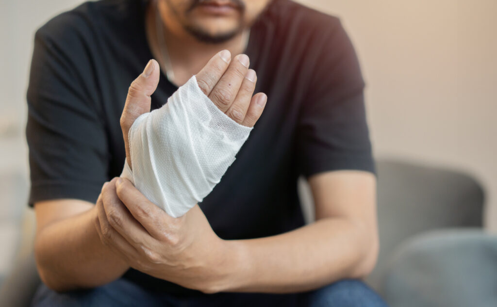 Close-up of a man with a beard and gray shirt holding his injured hand wrapped in gauze