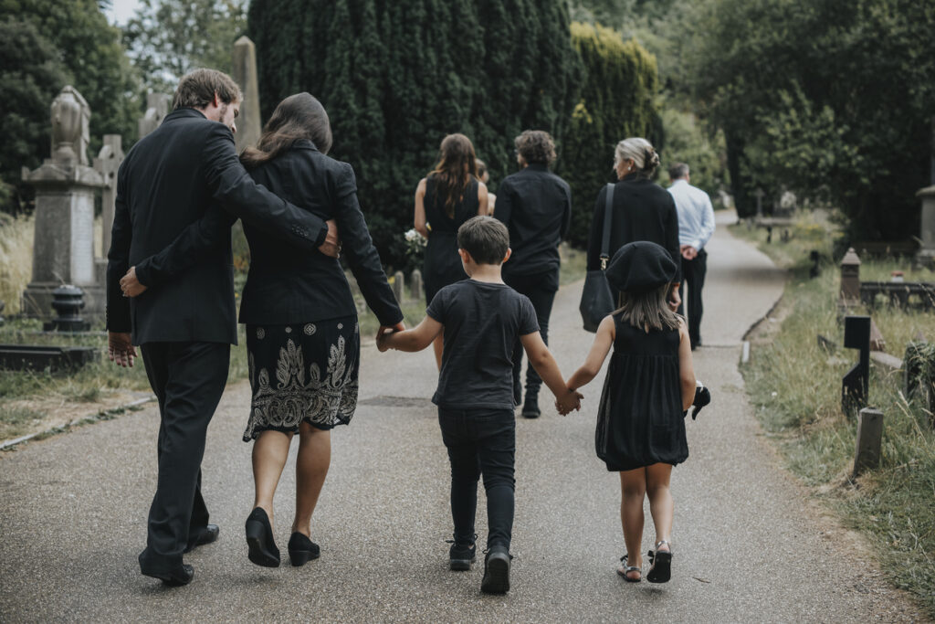 Rear view of a grieving family in black walking through a cemetery