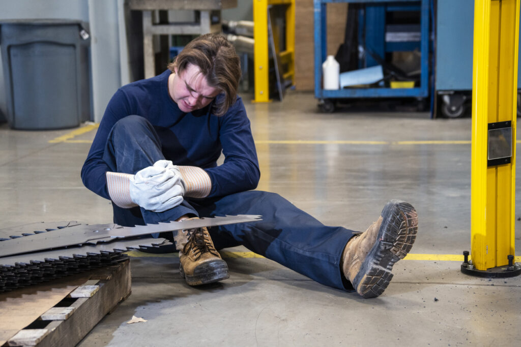 A worker holding his leg after being cut with serrated metal on the floor