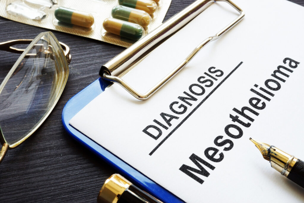 Close-up of a clipboard with a paper that says diagnosis mesothelioma and eyeglasses, yellow and green capsules, and a black pen