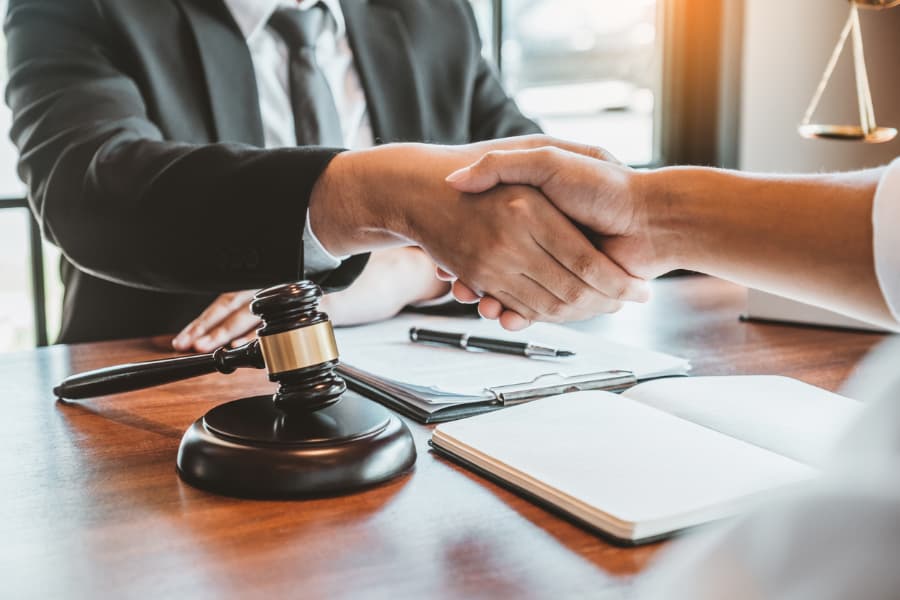 Close-up of men shaking hands over a desk with a gavel, pen and paper on it