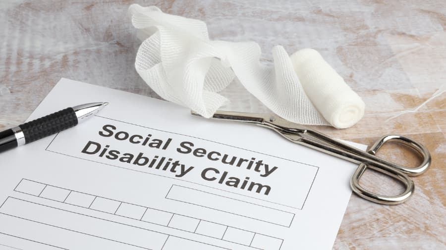 Social Security Disability claim form with a black pen, hemostat, and gauze on a marble table.