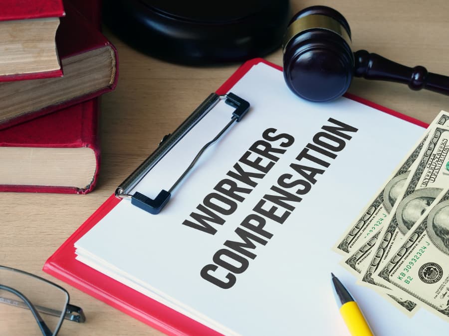 Workers’ compensation form with cash, pen, eyeglasses, books, and gavel