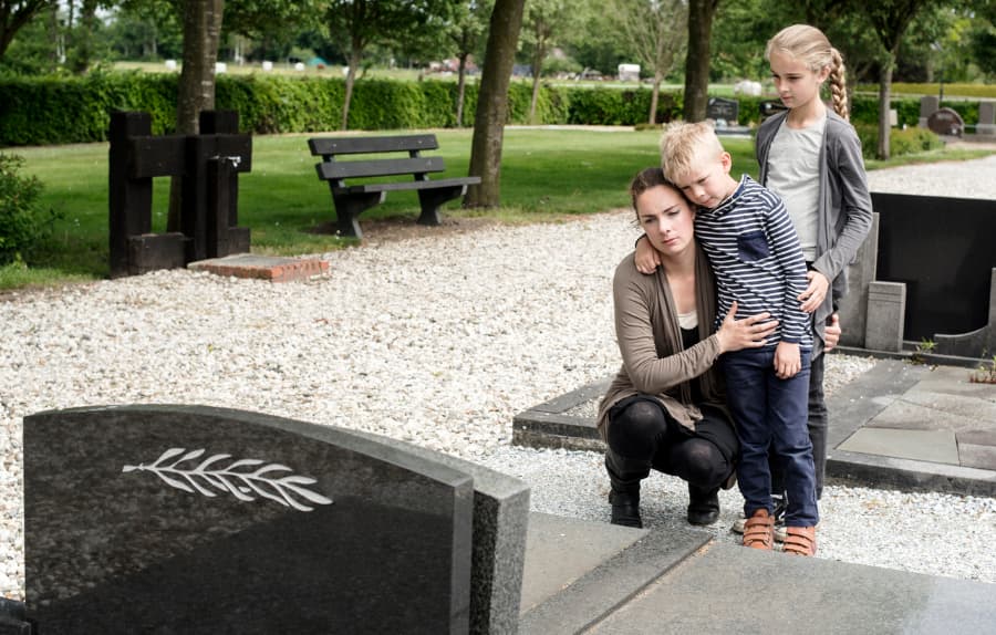 Young mother with children standing in front of the grave of a deceased loved one