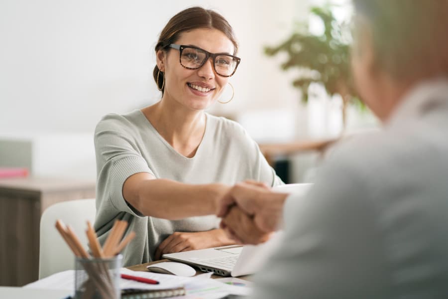 Woman with glasses sitting at a desk shaking hands with a male lawyer